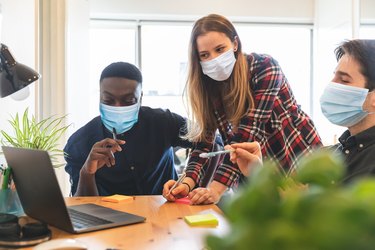 People wearing face mask at work in small home office - New working situation, business smart working during coronavirus pandemic