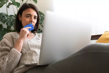 Pensive young woman in doubt holds credit card wondering if buying online.Checking online bank account. Copy space.