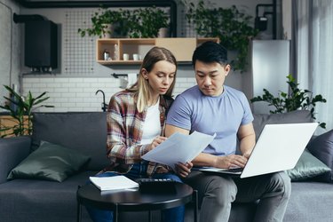 Young multiracial family, Asian man and woman, together at home, focused on home finances, pay bills online, using a laptop