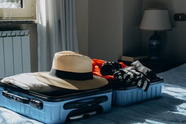 Summer clothes in a suitcase luggage for travel, Shadow Overlay . French style T-shirt with stripes and straw summer hat.