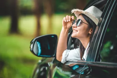 Happy woman hand holding hat outside open window car with meadow and mountain lake background. People lifestyle relaxing as traveler on road trip in holiday vacation. Transportation and travel concept