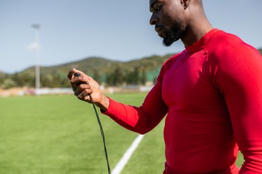 Side view of black sportsman in a football field checking times with a stopwatch.