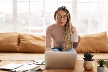 Successful african young businesswoman working on her laptop at home. Charming female student looking at computer screen watching webinar or doing video chat by webcam.
