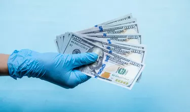 Hands in gloves holding a pack of dollars. Concept of paid medicine, treatment fees, bribes or illegal surgery. Copy space.
