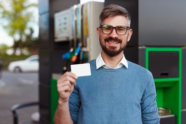 Cheerful man with blank card on gas station