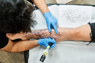 Top view of an unrecognizable tattoo artist tattooing an octopus design on his client's leg.