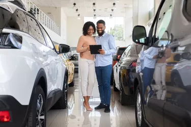 Young Black Couple Choosing Car In Modern Dealership Center, Checking Vehicle Characteristics