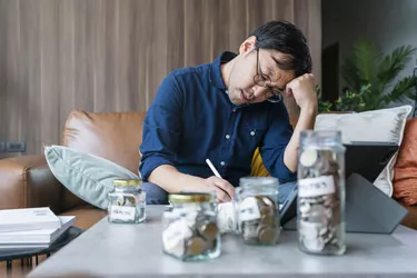 Upset frustrated young asian male calculate money saving sit at home table, depressed stressed guy worried about high bill tax invoice, overdue debt notification money problem