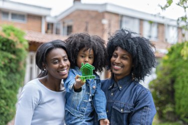 Afro-latin family, made up of mom and dad and a girl, pose smiling at the door of their new home.