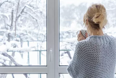 A woman looks out of the window at the snow-covered outdoors