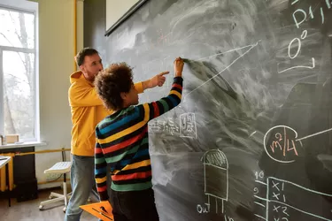 The great aim of education is not knowledge but action. Young male science teacher explaining main rules and formulas in physics and mechanics. A boy is drawing on the blackboard