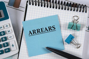 ARREARS - word on a blue piece of paper against the background of a notebook, calculator and pen