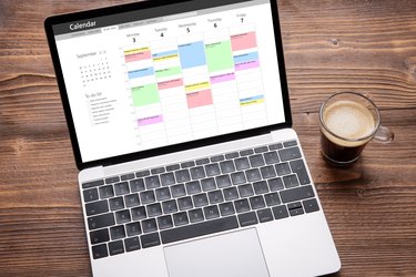 Laptop with calendar app on screen filled with different weekly appointments, meetings and tasks