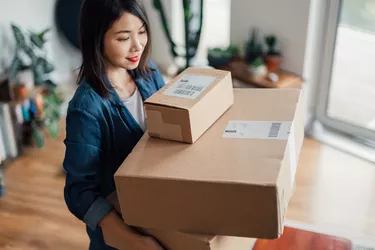 Young Asian freelance businesswoman carrying a stack of delivery boxes