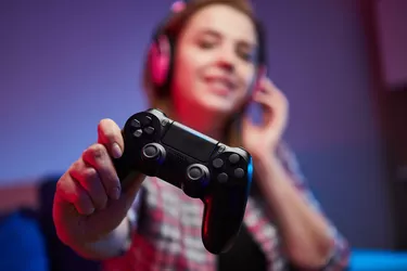 Portrait of crazy playful Gamer enjoying Playing Video Games on Playstation indoors sitting on the sofa, holding Console Gamepad in hands, Xbox fans. Resting At Home, have a great Weekend