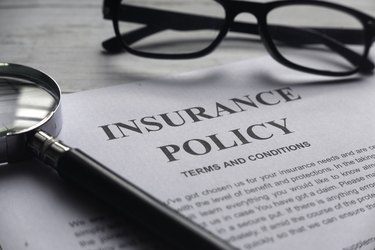 Selective focus of magnifying glass,glasses and Insurance Policy letter on a white wooden background.