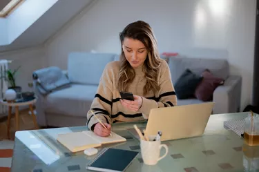 Woman using smartphone while working at home and using a laptop