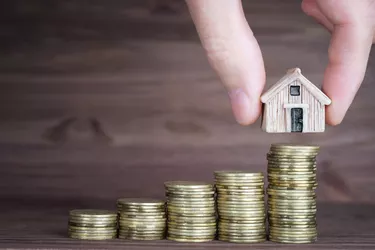 Putting a miniature house on a stack of coins