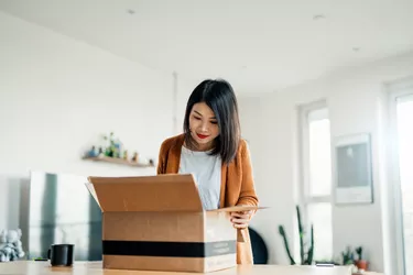 Smiling Young Woman Opening A Delivery Box In The Living Room