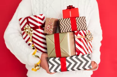 Heap of different gift boxes in hands of woman in white sweater against red wall. New Year celebration concept. Front view