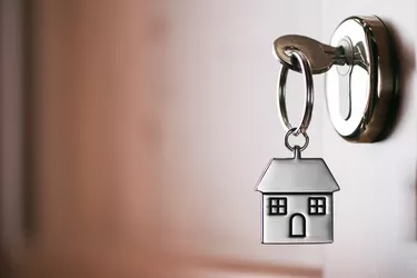 House key on a house shaped silver keyring in the lock of a entrance  brown door