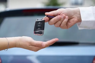car dealer gives the customer the car keys with car in backgorund