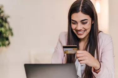 Laughing young adult businesswoman, looking at her debit card number.