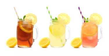 Three mason jars of summer iced tea, lemonade, and pink lemonade drinks isolated on white