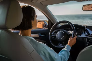 Woman sitting at the car and riding to the new places while traveling through the seashore