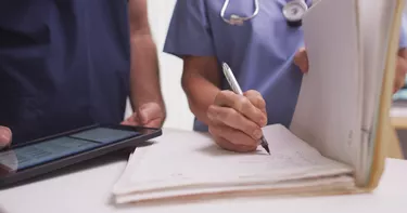 Close-up of mature female nurse writing in a patient's folder