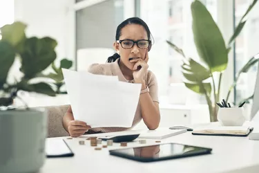 Shot of a young businesswoman looking stressed out while calculating finances in an office