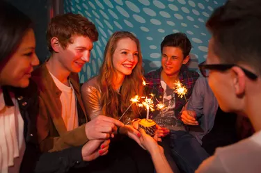 Group of teenagers sitting around birthday cake with sparklers