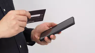 Hand is holding smart phone and black credit card on white background.