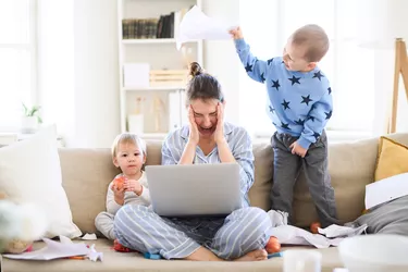 Stressed and frustrated mother with two small children in pajams working in home office, quarantine concept.