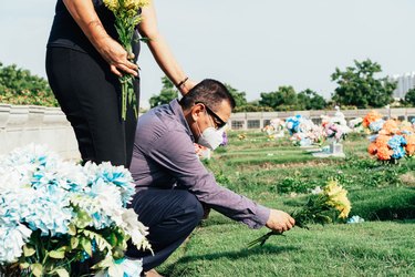 Sad Latino couple with medical mask at cemetery.