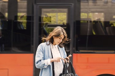 Young woman using mobile phone against bus