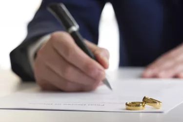 Hands of wife, husband signing decree of divorce, dissolution, canceling marriage, legal separation documents, filing divorce papers or premarital agreement prepared by lawyer. Wedding ring