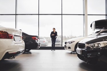 Full length of woman standing amidst cars in showroom