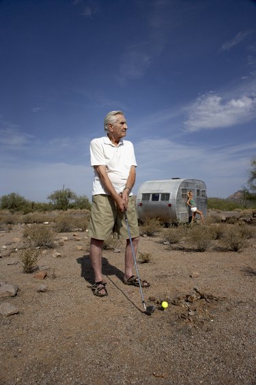Man playing golf in desert and teenage girl (14-15) leaning on trailer in background