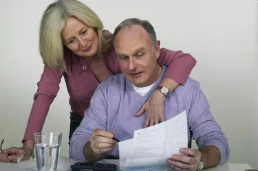 Mature woman with arm around mature man at desk pointing to bill