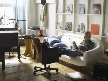 Mature man sitting on sofa, reading newspaper