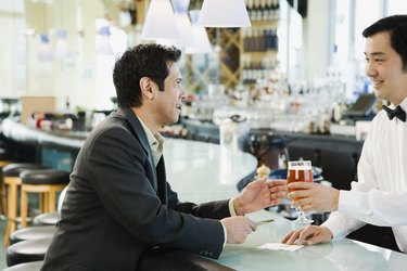 Male bartender serving man drink at bar