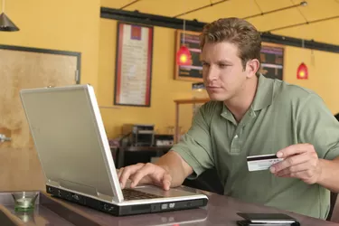 Close-up of a young man using a laptop and holding a credit card for online shopping
