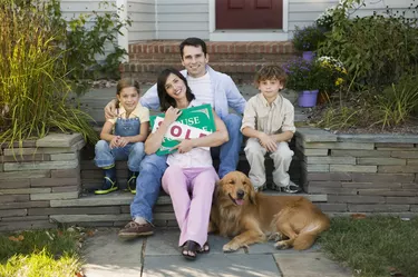 Family sitting next to house with a sold sign