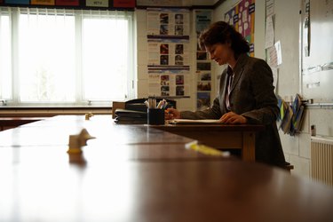 Mature female teacher marking papers at desk in classroom, side view