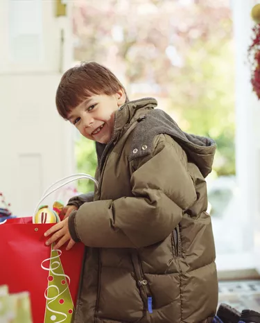 Boy (6-8) kneeling by bag in hall, smiling, portrait