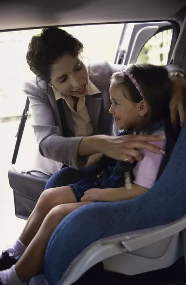 Mother placing her daughter in a car seat