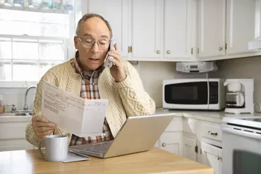 Senior man using computer and cordless phone