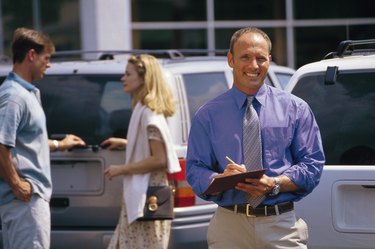 Car salesman on lot with couple
