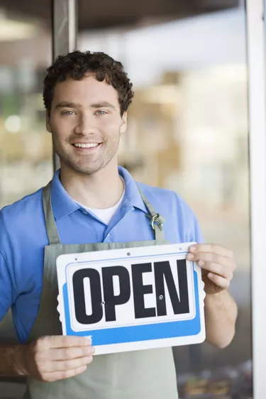 Shopkeeper smiling by storefront with open sign